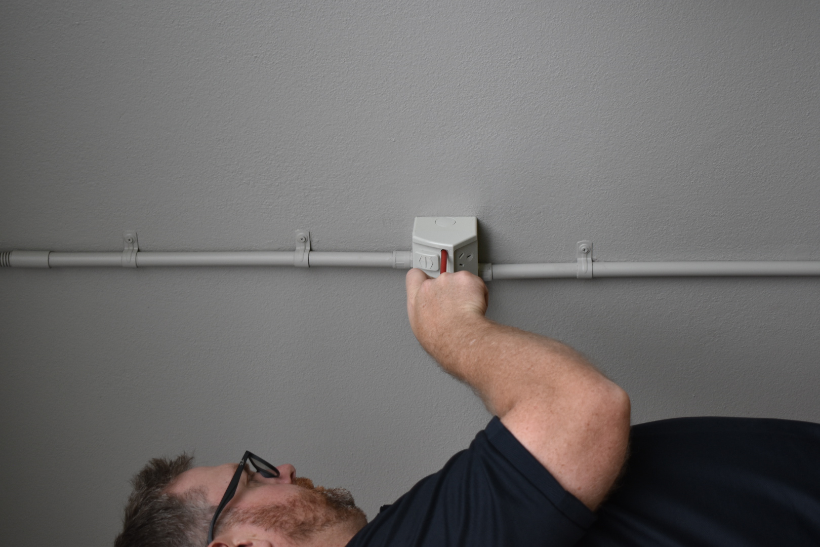 Electrician working on a wall-mounted power point with conduit