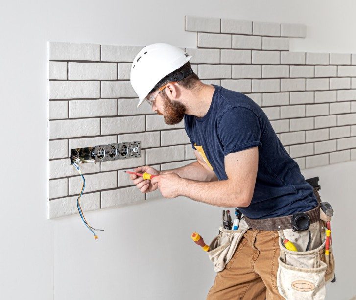 Electrician in a hard hat wiring a bank of power points into a wall