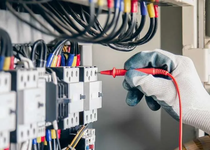 Gloved hand testing a switchboard circuit with a multimeter probe